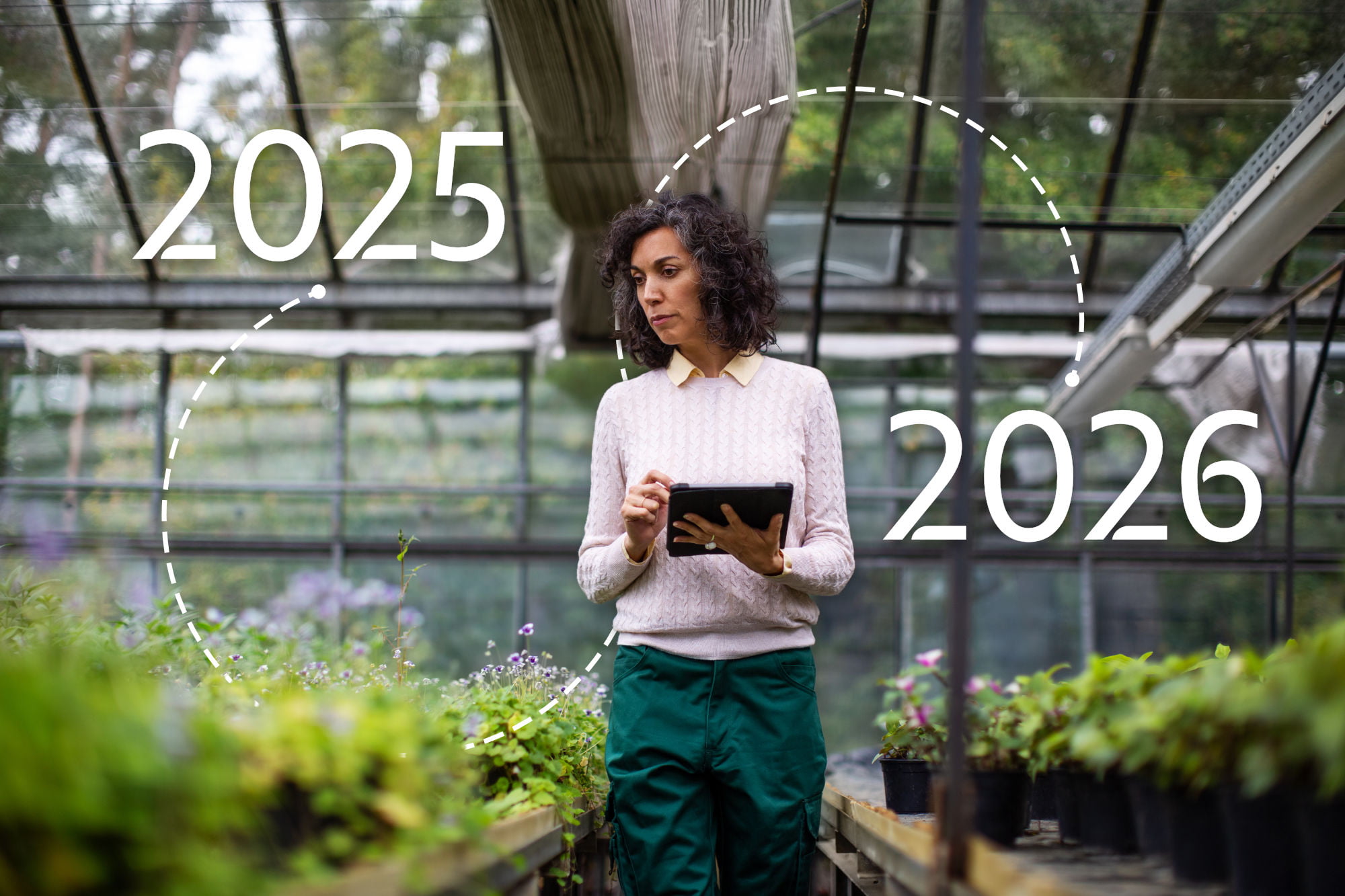 En person står i et drivhus mellom rekker av grønne planter og holder et nettbrett. Over bildet vises tallene «2025» og «2026», koblet sammen med en stiplet linje som antyder overgang eller planlegging over tid.