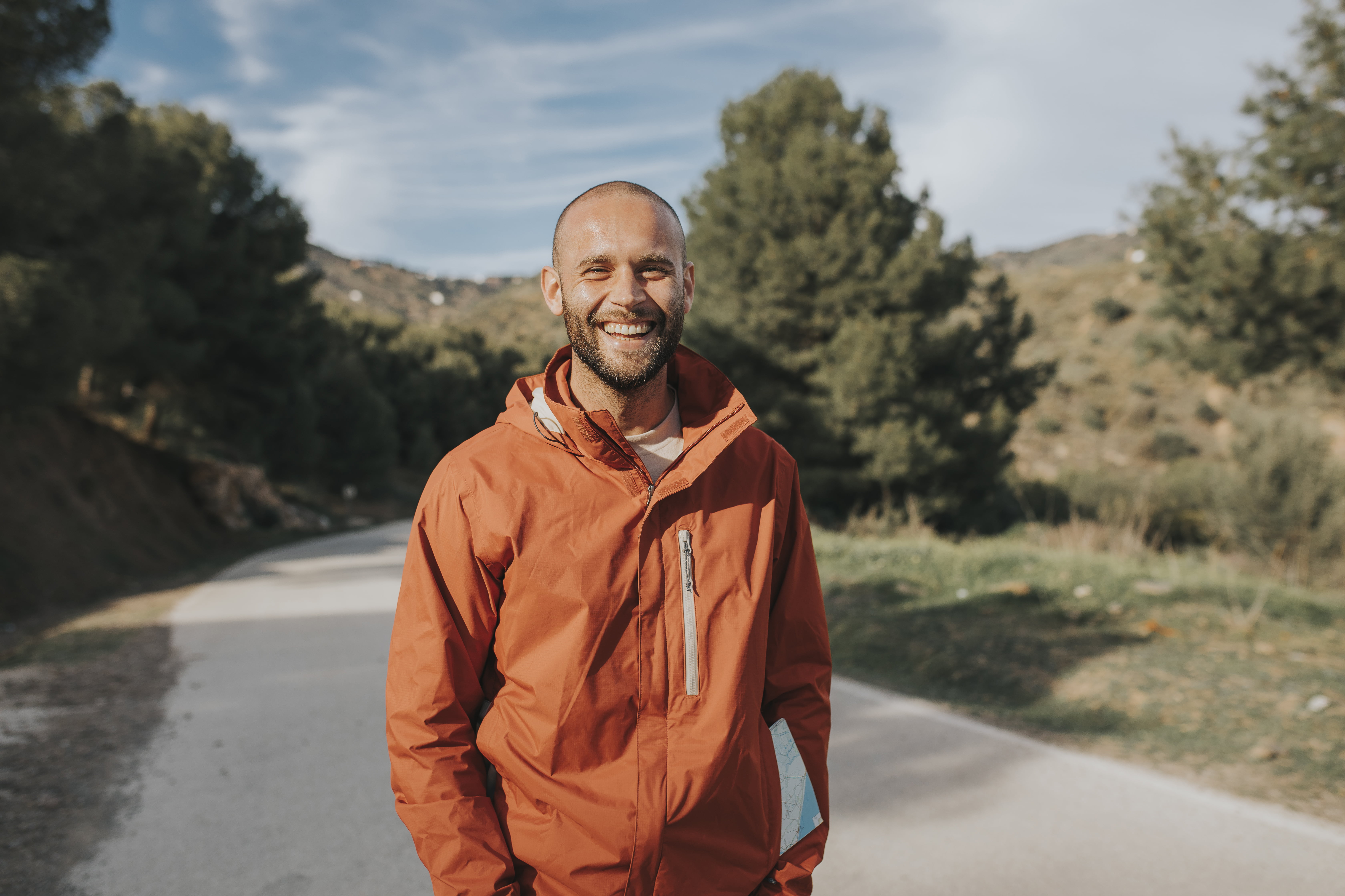 Ung mann som står smilende med hendene i lommen ute i naturen